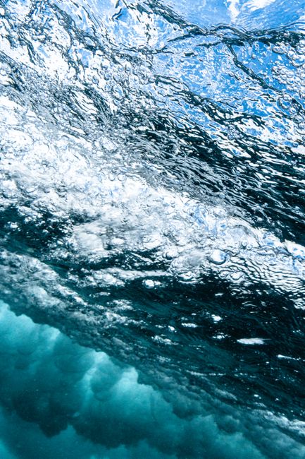 From below of textured background of wavy sea water with shiny blue and white surface in daylight