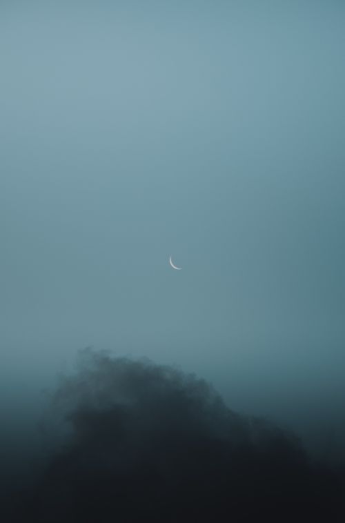 Free A crescent moon peeking through a misty, cloudy night sky. Serene and atmospheric setting. Stock Photo