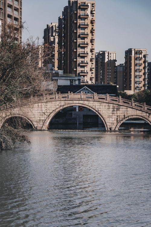 Free Cityscape of old bridge over rippling river near modern urban buildings in cloudy day in fall Stock Photo