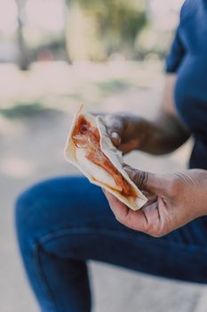 Close-up of a person holding a delicious bacon and egg wrap outdoors, highlighting a casual meal setting.