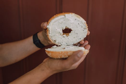Person holding a freshly sliced bagel with cream cheese, perfect for breakfast or snack.