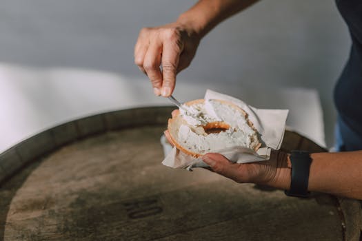 A person spreads cream cheese on a bagel in natural light, highlighting a simple breakfast moment.