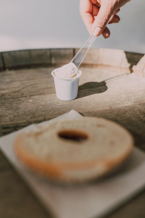 Free A hand spreading cream cheese on a fresh bagel on a wooden surface. Stock Photo