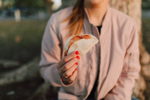 A woman enjoys a hand-held taco in a serene outdoor setting, perfect snack choice.