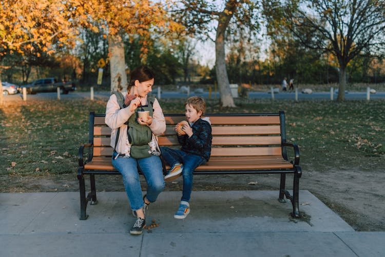 Mother And Child Sitting On A Wooden Bench While Eating 