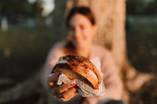 Close-up of a woman holding a sandwich outdoors during warm daylight.