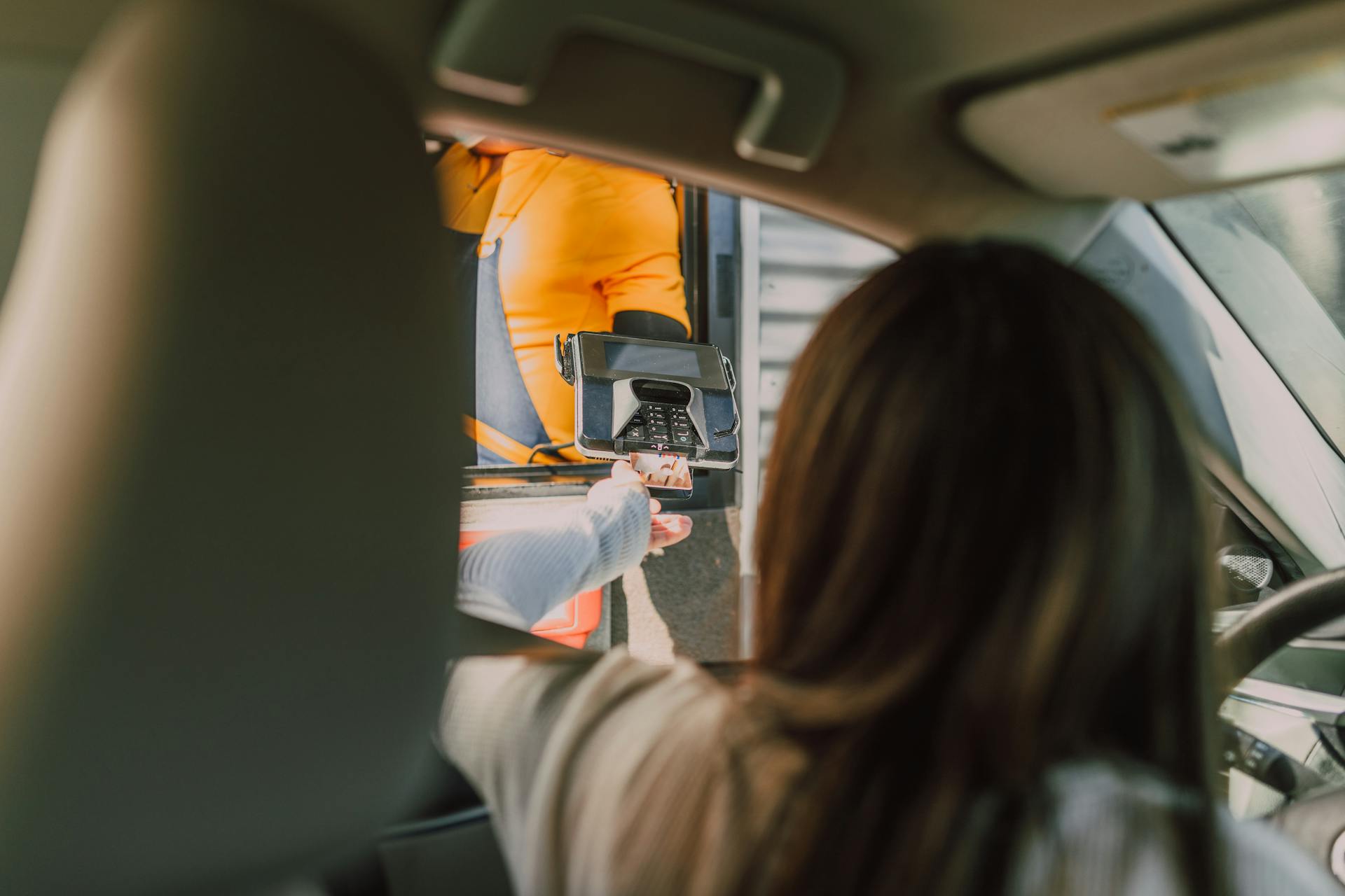 Customer makes a contactless payment at a fast-food drive-thru from a car.