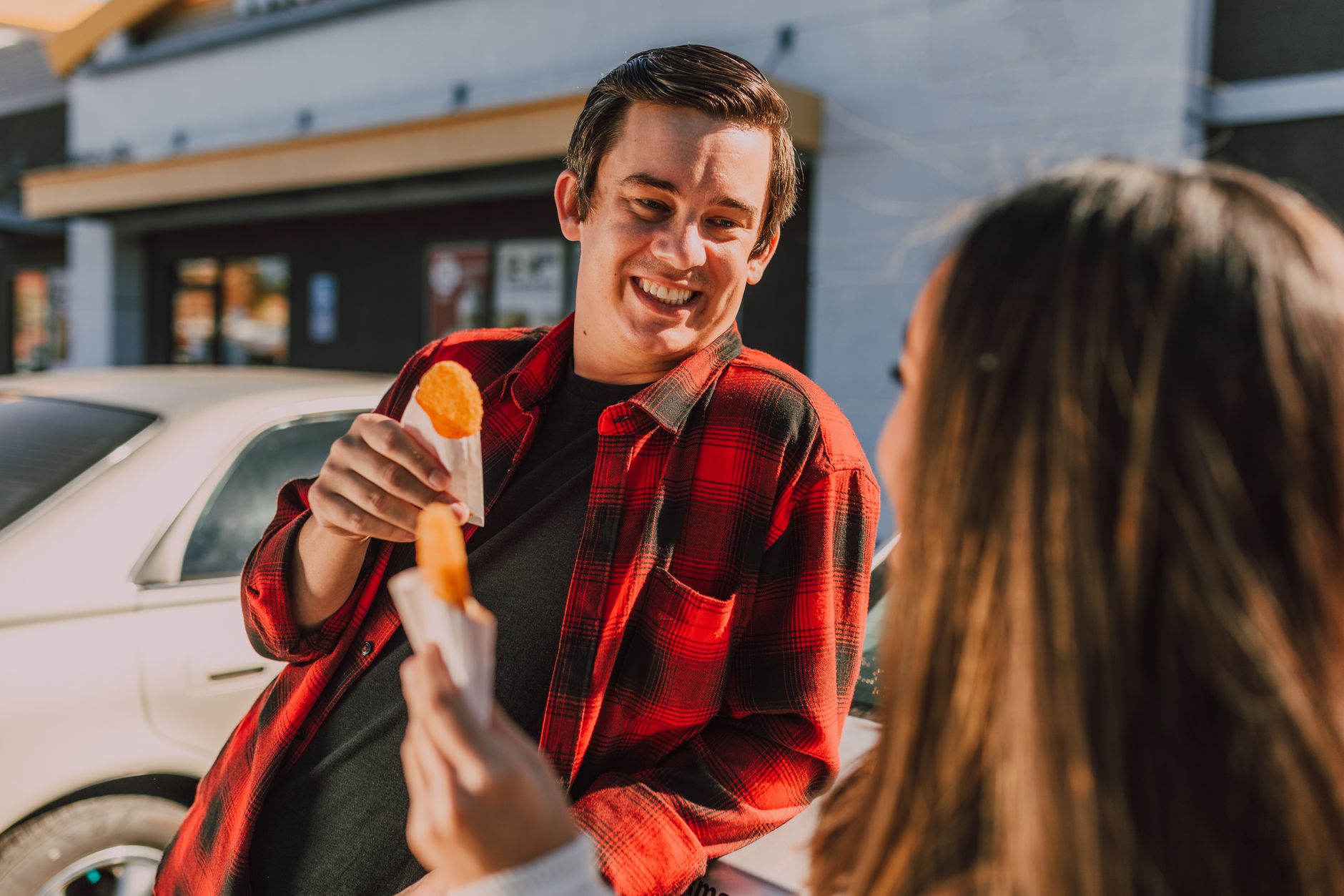 Des amis souriants partagent des hash browns dans une scène extérieure joyeuse.