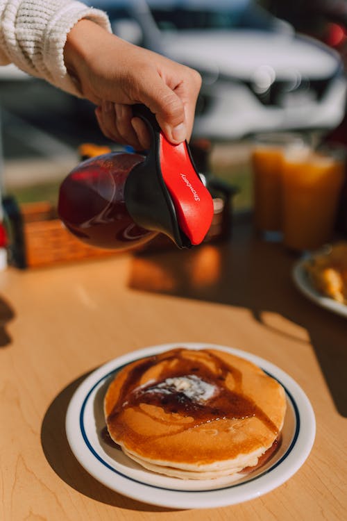 Person Pouring Syrup on Her Pancakes