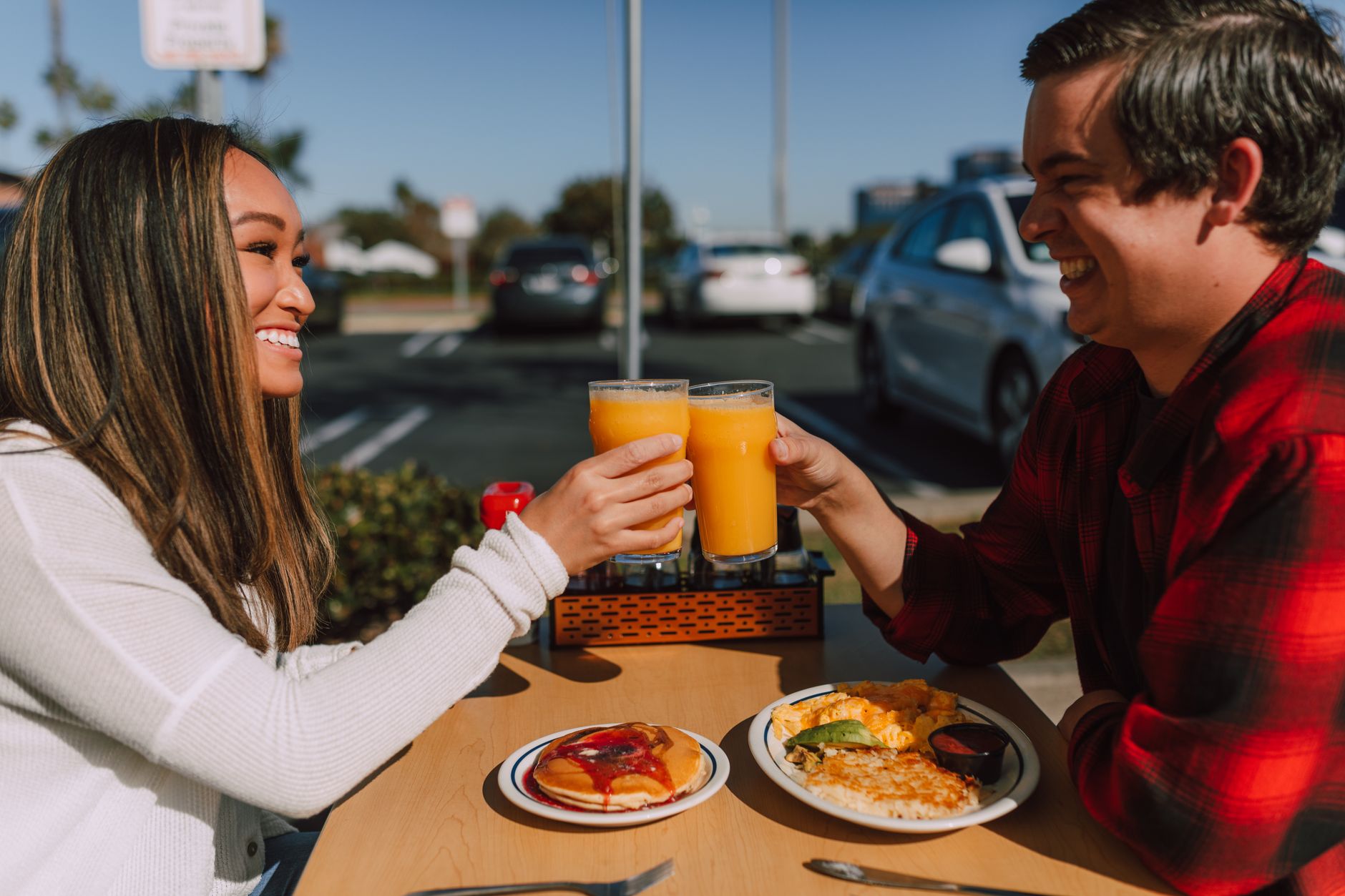 Smiling couple toasting with orange juice while having brunch at an outdoor cafe. Sunny day joy.