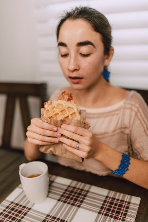 Woman in Brown Long Sleeve Shirt Holding a Waffle Sandwich