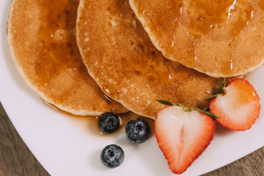 Plate of pancakes with strawberries, blueberries, and syrup, perfect for breakfast.