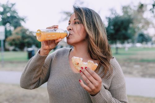 Free Woman enjoying a bagel and orange juice in a park, capturing a fresh morning vibe. Stock Photo