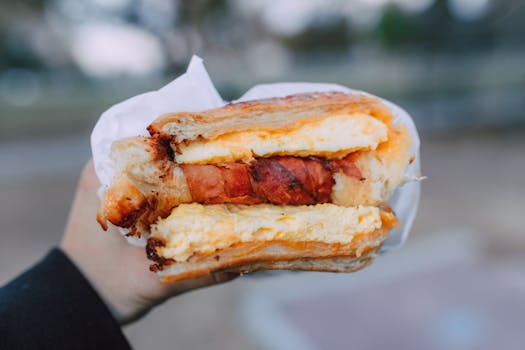 Close-up of a delicious breakfast sandwich with cheese and bacon held outside.