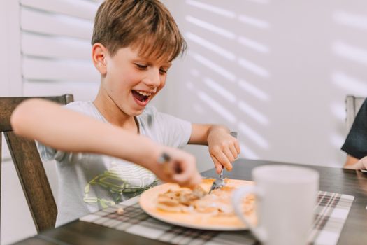 Happy child eating breakfast, cutting food with joy and enthusiasm at the dining table.