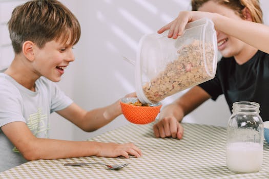 Two happy kids pouring cereal into bowls, enjoying a cheerful breakfast at home.
