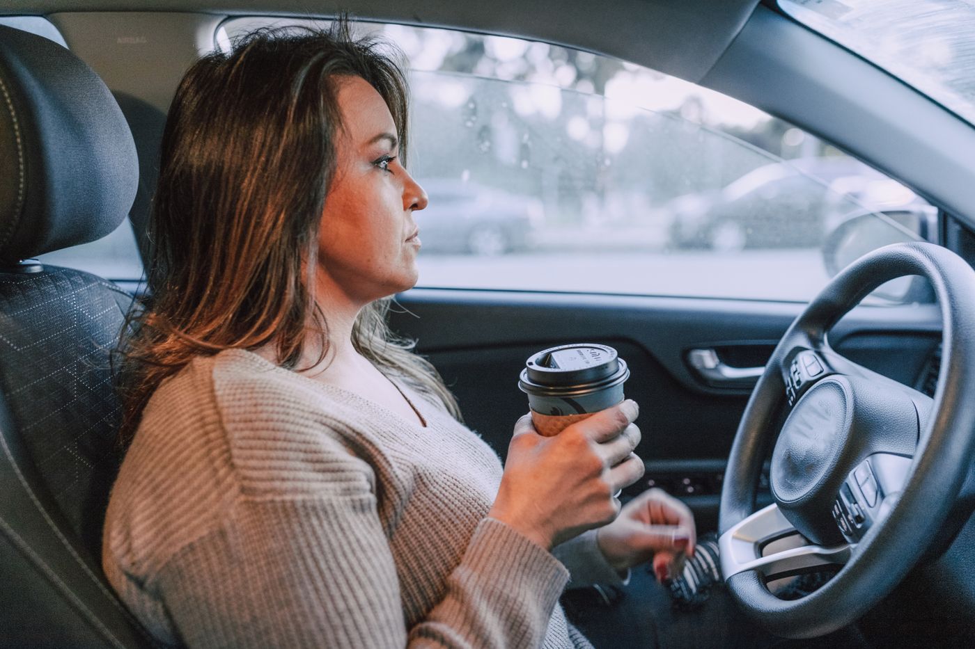 A driver holding a takeaway coffee with her seatbelt on, eyes on the road