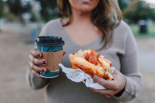 A Woman Holding a Sandwich and a Cup of Coffee