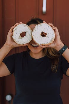 Smiling woman holding bagels with cream cheese playfully over her eyes.