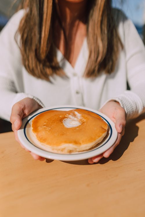 Free Close-up of a woman serving a buttered pancake on a sunny morning. Ideal for food blogs. Stock Photo