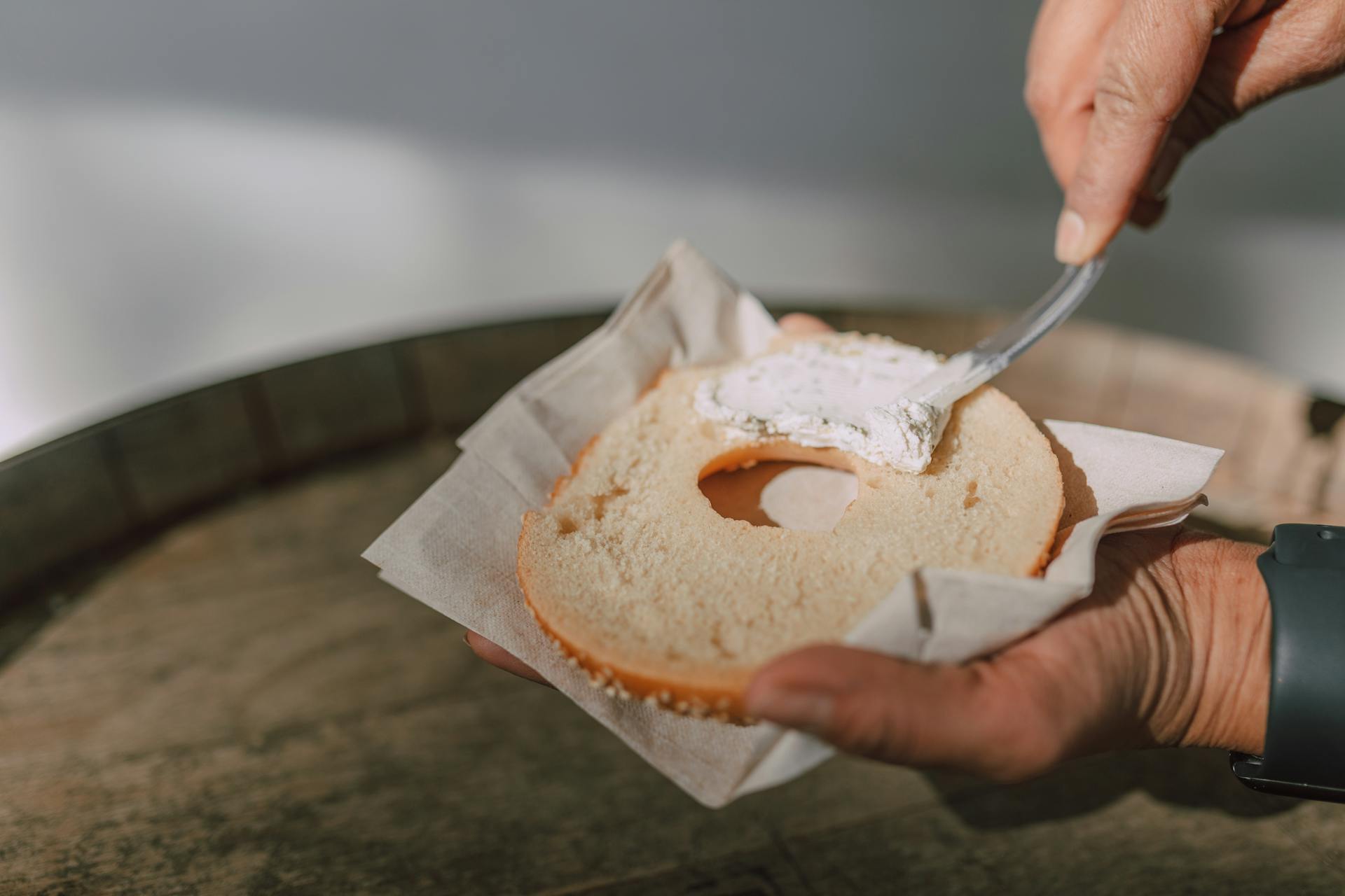 Close-up of hands spreading creamy cheese on a sliced bagel.