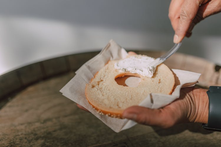 Person Spreading Cream Cheese On A Bagel