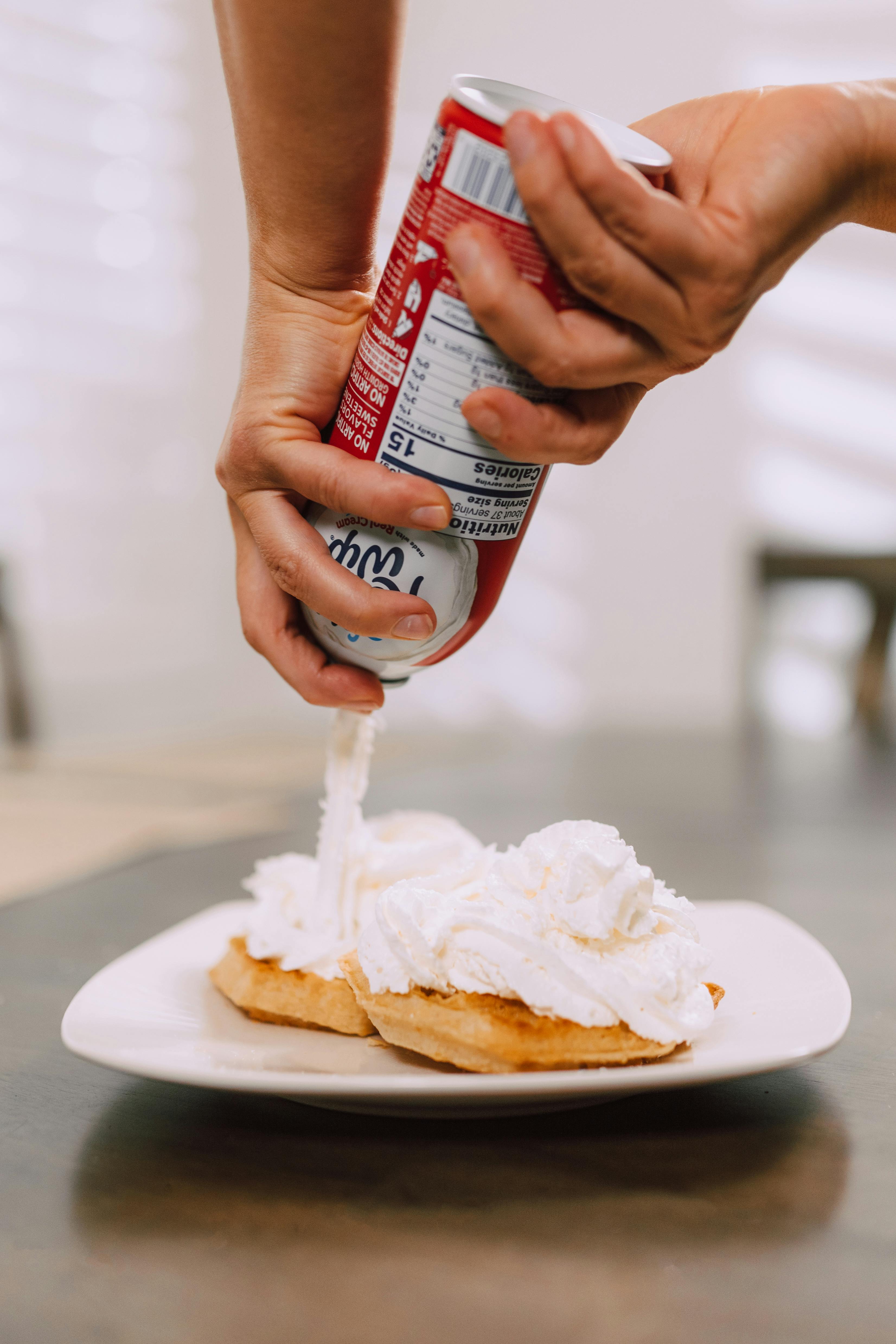 person pouring whipped cream on bagels