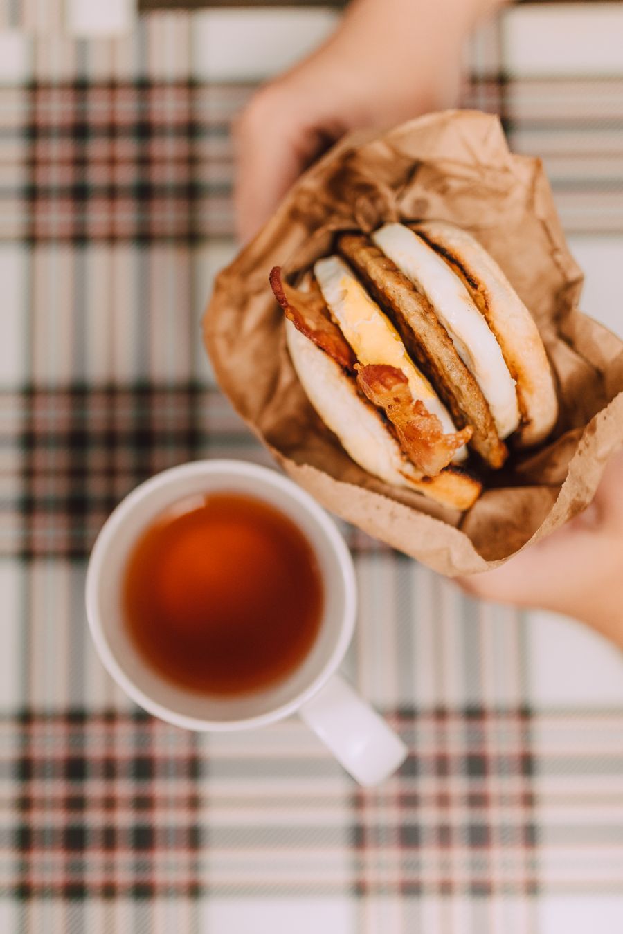 A bacon and egg breakfast sandwich with a cup of tea
