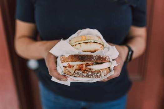 Close-up of a person holding two appetizing sandwiches wrapped in paper.