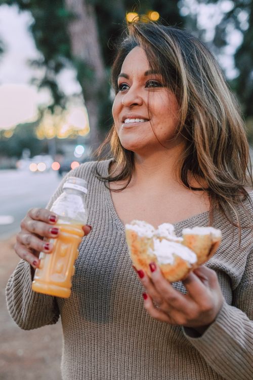 Free Smiling woman holds a cream cheese bagel and fruit juice outdoors, capturing a delightful breakfast moment. Stock Photo
