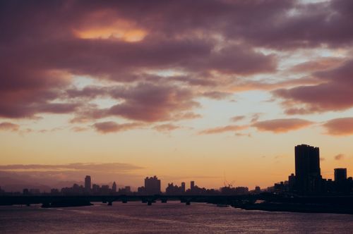 Free Silhouette of a city skyline with a cloudy sky at twilight, reflecting on the river. Stock Photo