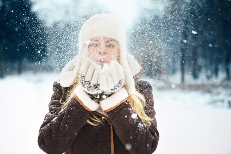 Beautiful Woman In Winter Clothing Blowing Snow On Her Hands