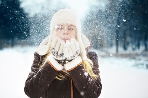 Free Woman in winter clothing blowing snow, creating a magical winter atmosphere. Stock Photo