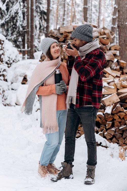 Free Happy couple drinking hot beverages in snowy forest, embracing winter warmth. Stock Photo