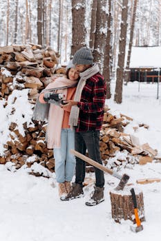 Romantic couple dressed in winter clothing collecting firewood in a snowy forest setting.