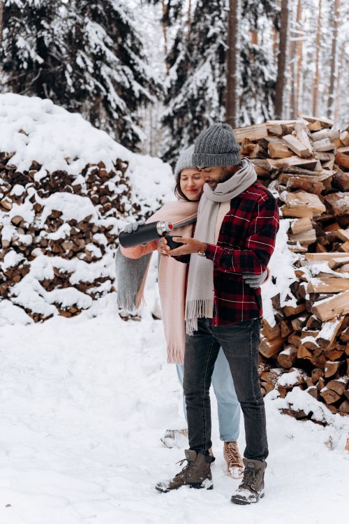 Free Cozy couple in winter clothing enjoying snow in the forest, showcasing love and togetherness. Stock Photo