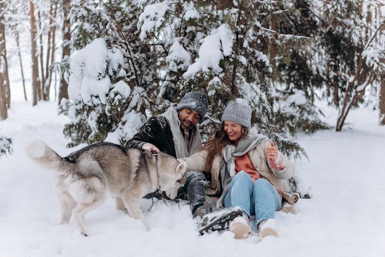 A Couple Playing With Their Dog In The Snow