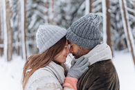 A couple shares an intimate moment in a snowy forest, embracing warmth and love.