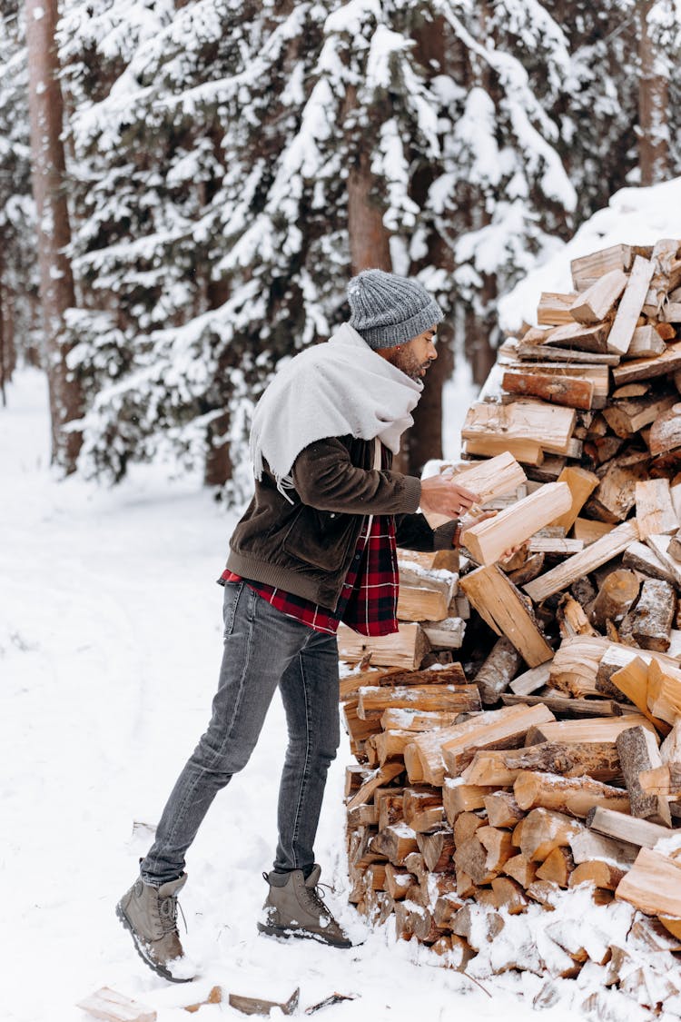 A Man Stacking Firewood In A Winter Forest