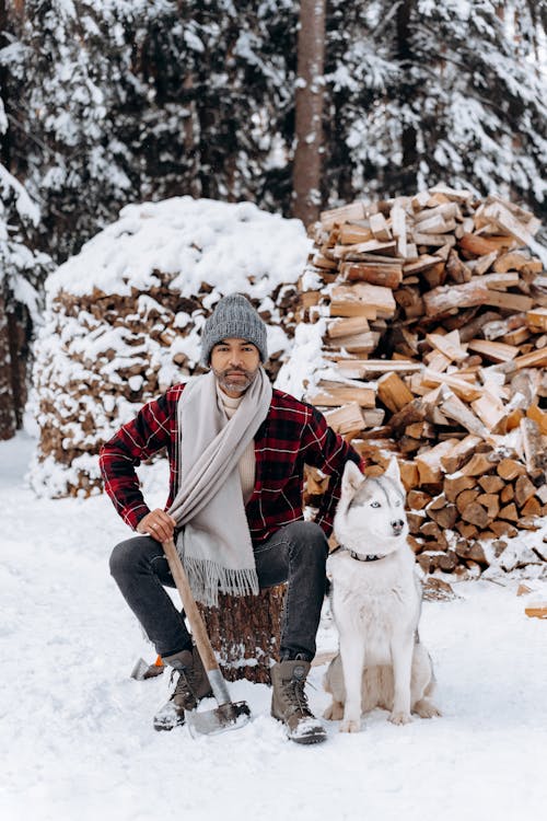 Woman in Red and Black Plaid Coat Holding Brown Wooden Stick Near White Short Coat Dog