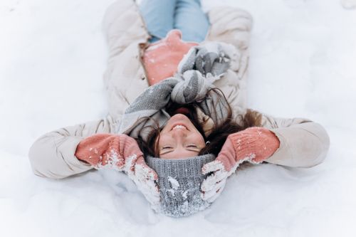 Free Caucasian woman lying happily on snow in winter attire, smiling warmly. Stock Photo