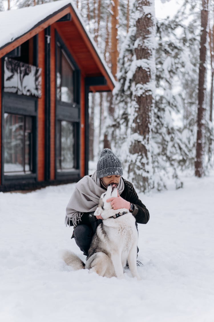 A Man Hugging His Dog While Sitting In The Snow