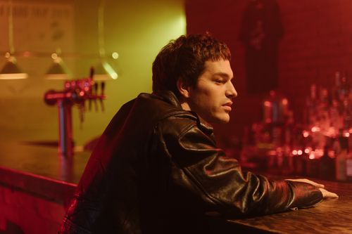 Free A young man in a leather jacket sits thoughtfully at a dimly lit bar counter. Stock Photo