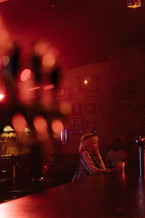 Free A woman sits alone at a dimly lit bar counter with a moody atmosphere. Stock Photo