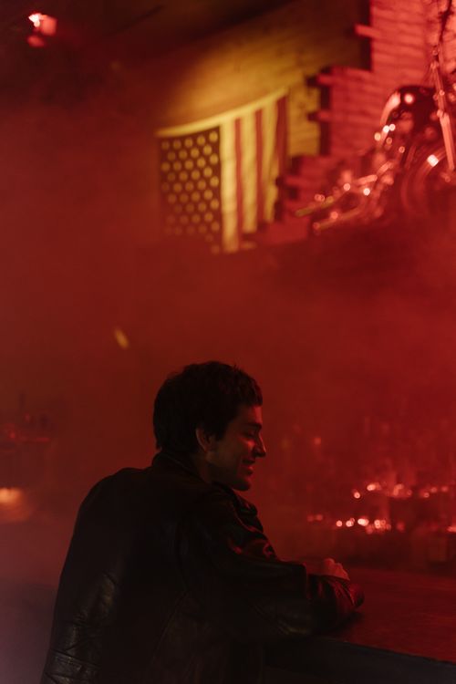 Free A person in a black jacket sits at a bar with dim lighting and smoke. Stock Photo