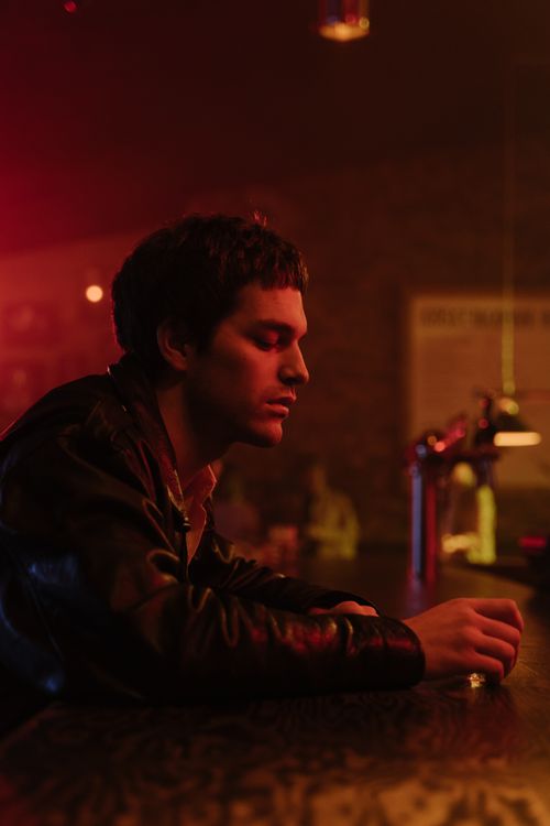 Free A contemplative man sits alone at a dim bar, holding a drink, deep in thought. Stock Photo