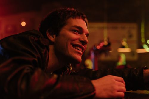 Free Side view of a young man smiling in a bar with warm ambient lighting and blurred background. Stock Photo