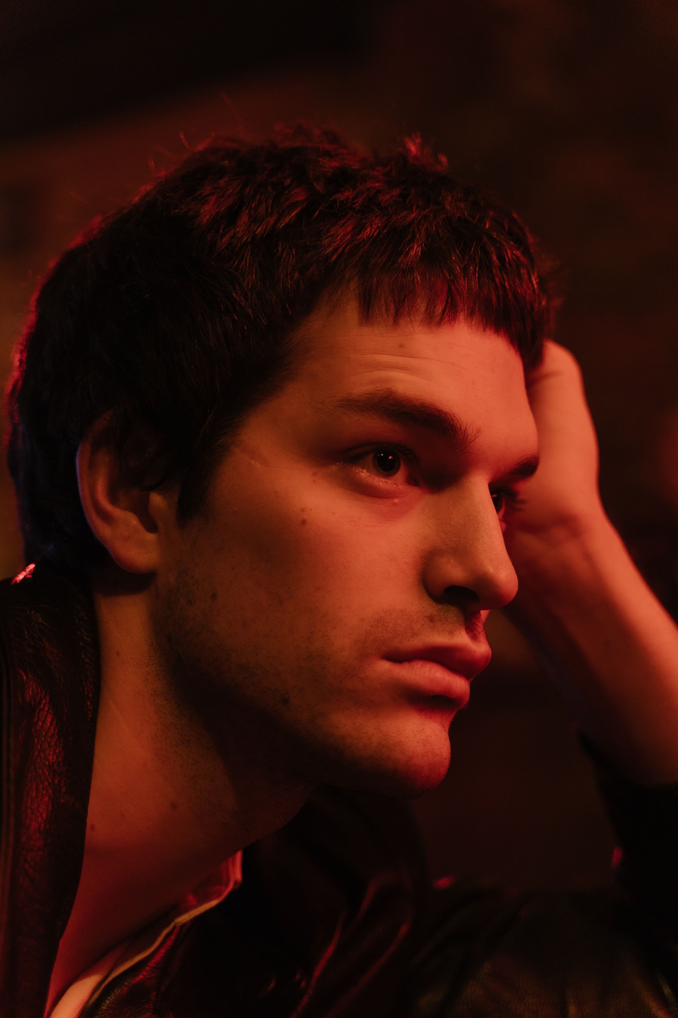Close-up side view of a young man in a contemplative pose with warm lighting.