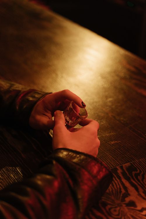 Free Cozy ambiance with hands holding a shot glass on a wooden bar table. Stock Photo