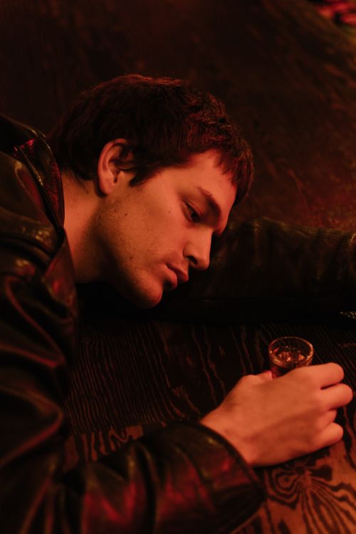 Free A man in a leather jacket holds a drink, reflecting in a dimly lit setting. Stock Photo